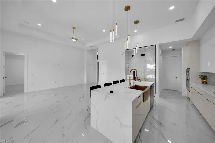 Kitchen with a kitchen island with sink, a tray ceiling, white cabinets, and decorative light fixtures