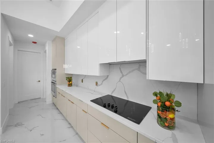 Kitchen with light tile floors, light stone countertops, tasteful backsplash, and black electric cooktop