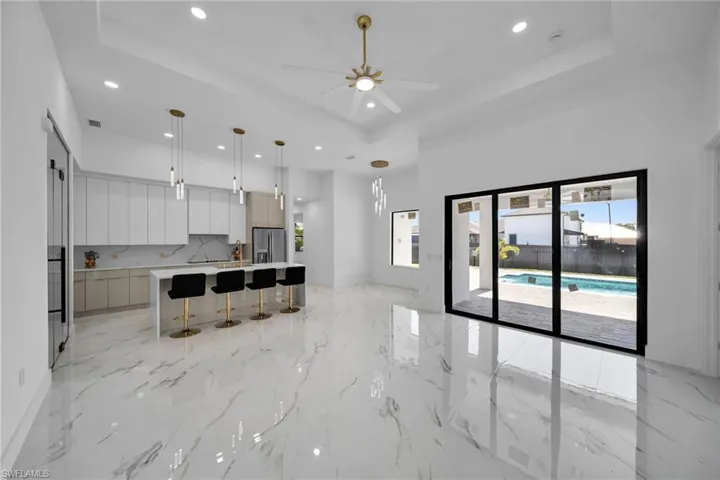 Kitchen with ceiling fan, a tray ceiling, stainless steel fridge, light tile flooring, and a center island