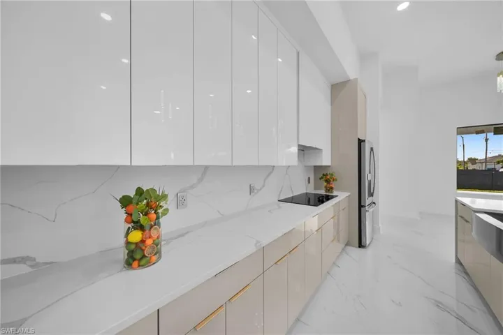 Kitchen featuring black electric stovetop, backsplash, light stone countertops, stainless steel fridge, and light tile floors