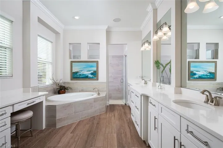 Bathroom with ornamental molding, double vanity, a garden tub, wood finished floors, and a stall shower