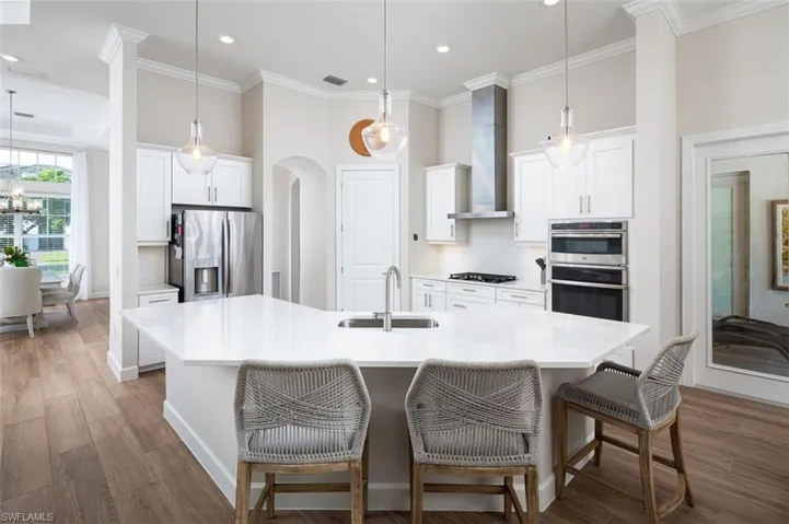 Kitchen featuring crown molding, stainless steel appliances, wood finished floors, a kitchen bar, and an island with sink
