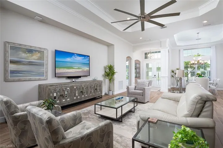 Living room featuring crown molding, a raised ceiling, recessed lighting, french doors, and arched walkways