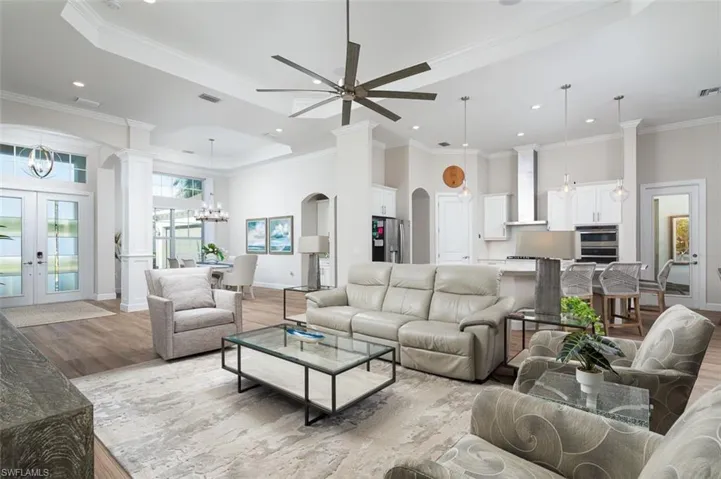 Living area with a chandelier, ornamental molding, light wood finished floors, arched walkways, and french doors