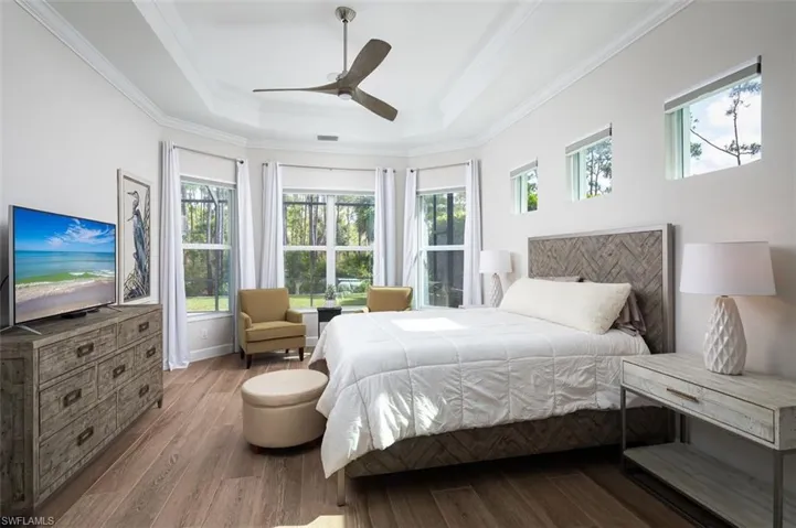 Bedroom with wood finished floors, ornamental molding, a tray ceiling, and a ceiling fan