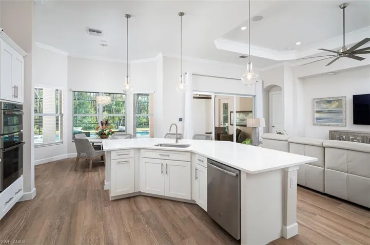 Kitchen with open floor plan, appliances with stainless steel finishes, crown molding, light countertops, and wood finished floors