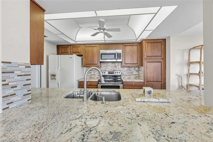 Kitchen with brown cabinets, backsplash, stainless steel appliances, and light stone counters