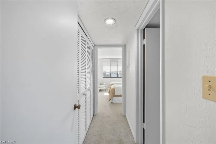 Hall with light colored carpet, a textured ceiling, and a textured wall