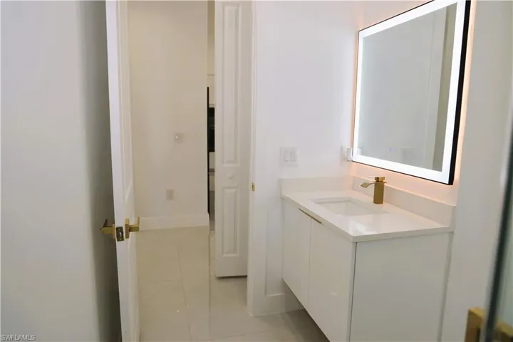 Floating white vanity with integrated sink, gold-tone faucet, and illuminated rectangular mirror