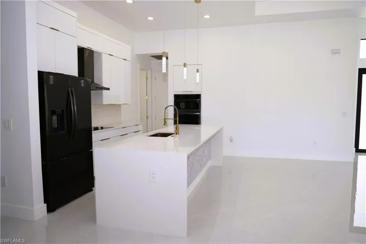 Kitchen featuring white cabinetry, a black refrigerator, a kitchen island with an undermount sink, pendant lighting, and tile flooring