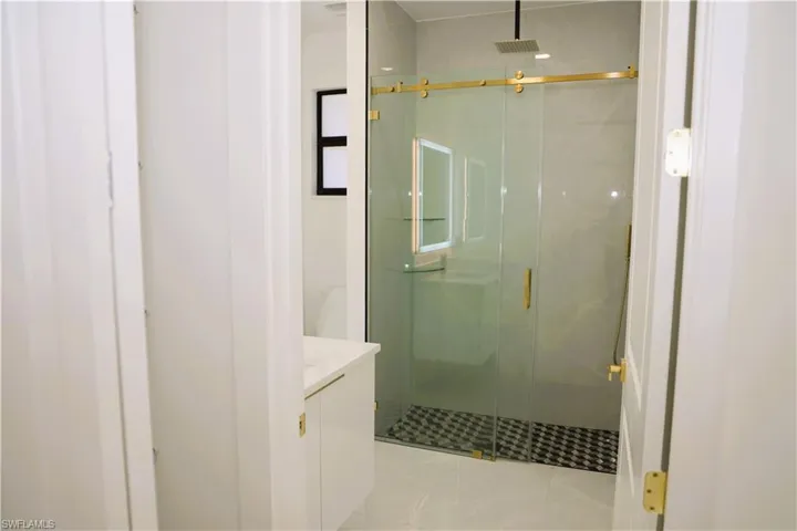 Glass-enclosed shower with gold-tone hardware, a rainfall showerhead, and a mosaic tile floor
