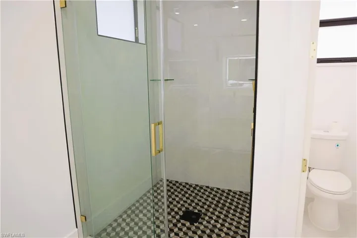 Frameless glass shower enclosure with brass hardware, black and white geometric tile shower floor, and contrasting white wall tiling