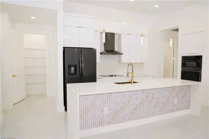 Modern kitchen featuring white cabinetry, a large center island with a decorative facade, integrated black appliances, and a walk-in pantry
