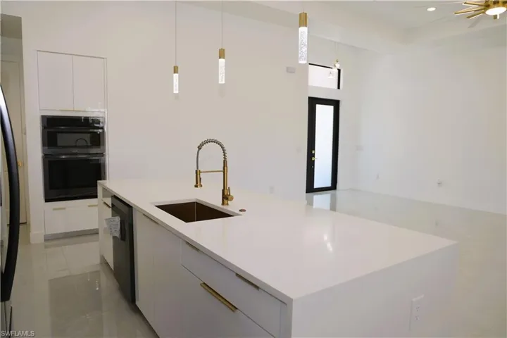 Kitchen island with a white countertop and gold-toned fixtures, built-in double oven, integrated dishwasher, and contemporary pendant lighting
