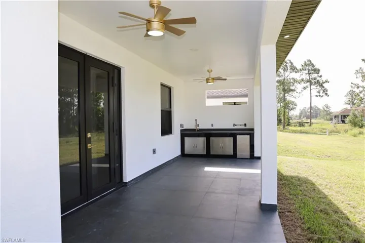 Covered outdoor patio with dark tile flooring, two ceiling fans, and an outdoor kitchen featuring a built-in sink and stainless-steel cabinetry