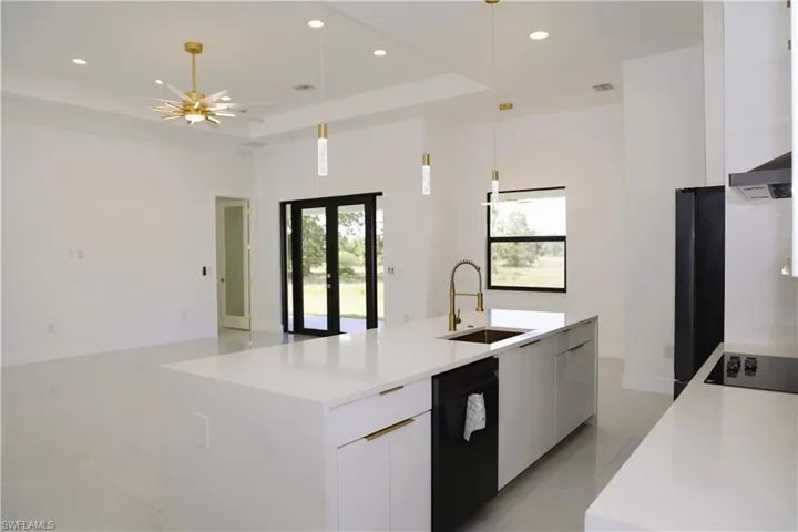Spacious kitchen island with an integrated sink, modern pendant lighting, sleek white cabinetry, and stainless steel appliances