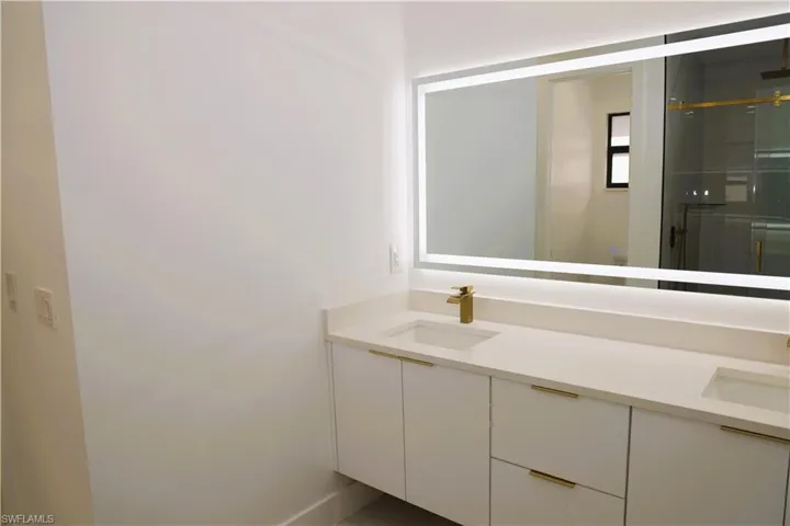Dual basin vanity with integrated sinks, light-toned countertop, gold-finish fixtures, and an illuminated mirror