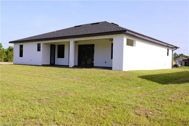 Stucco exterior with a dark shingle roof, covered patio, and dual glass panel doors