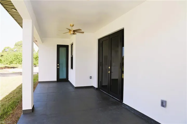 Covered patio with dark-toned flooring, white exterior walls, and a ceiling fan