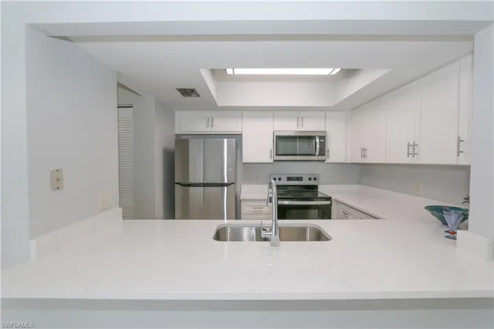 Kitchen featuring peninsula, quartz countertops, sink, white cabinets, appliances with stainless steel finishes appliances.
