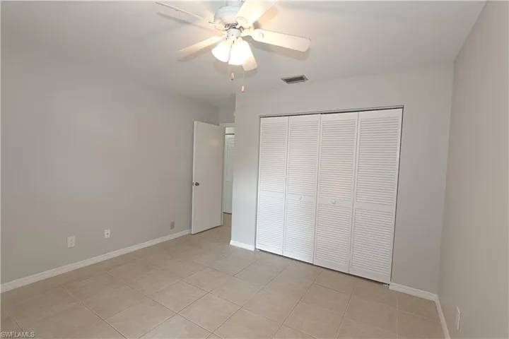 Guest bedroom with ceiling fan, light tile patterned floors and a closet.