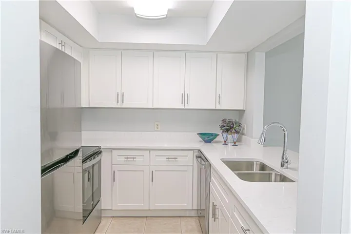Kitchen featuring, quartz countertops, light tile patterned floors, stainless steel appliances, a sink, and white cabinetry