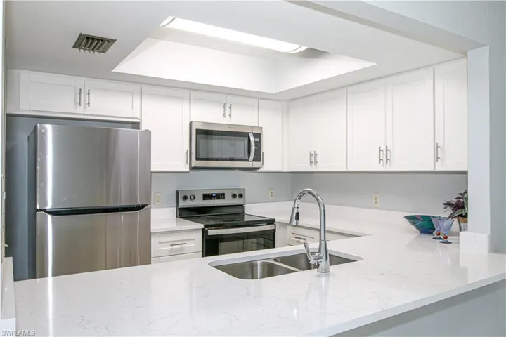 Kitchen featuring kitchen peninsula, appliances with stainless finishes a raised ceiling, sink and white cabinets