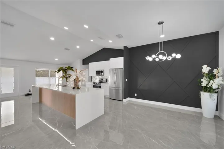 Kitchen featuring white cabinets, hanging light fixtures, a large island, light stone counters, and stainless steel appliances