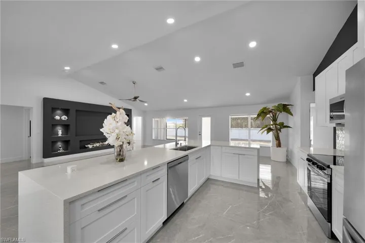 Kitchen featuring vaulted ceiling, appliances with stainless steel finishes, white cabinetry, sink, and light stone countertops