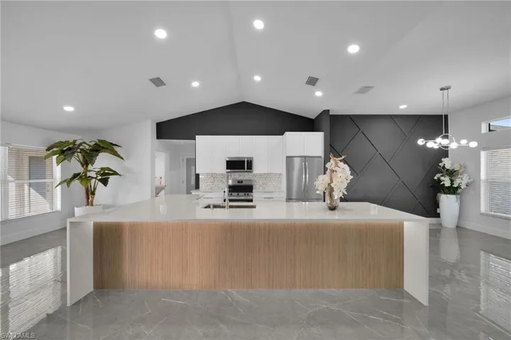 Kitchen featuring a spacious island, decorative light fixtures, vaulted ceiling, stainless steel appliances, and backsplash