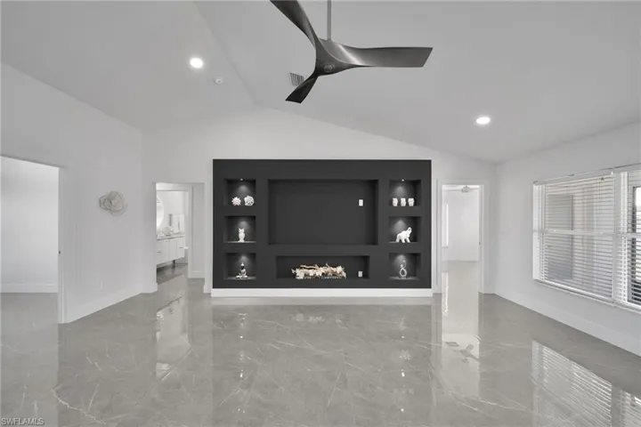 Unfurnished living room featuring lofted ceiling, built in features, and ceiling fan