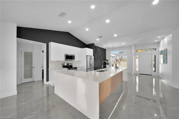 Kitchen featuring appliances with stainless steel finishes, tasteful backsplash, white cabinetry, sink, and a spacious island