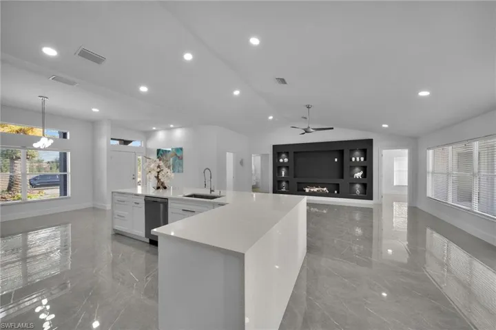 Kitchen featuring lofted ceiling, sink, decorative light fixtures, light stone countertops, and white cabinets