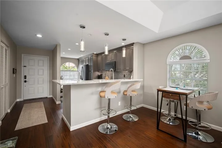 Kitchen with decorative backsplash, light stone counters, dark wood-type flooring, pendant lighting, and a kitchen breakfast bar