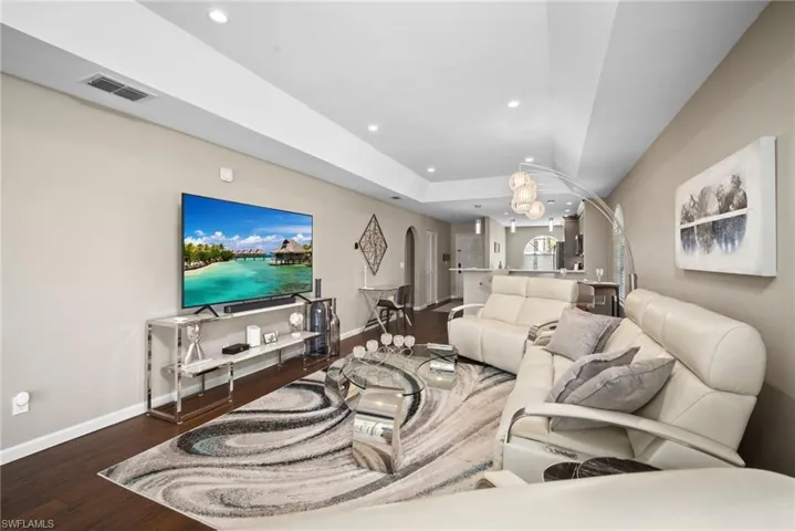 Living area featuring arched walkways, dark wood-type flooring, a tray ceiling, and recessed lighting