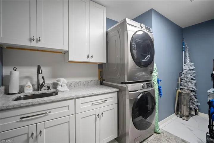 Laundry area with stacked washing machine and dryer, cabinet space, and marble finish flooring
