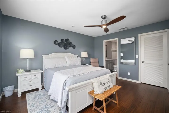 Bedroom with dark wood-style floors, ceiling fan, and ensuite bath