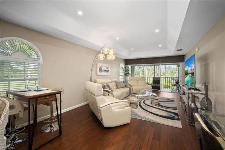 Living room with a raised ceiling, dark wood-style floors, and recessed lighting