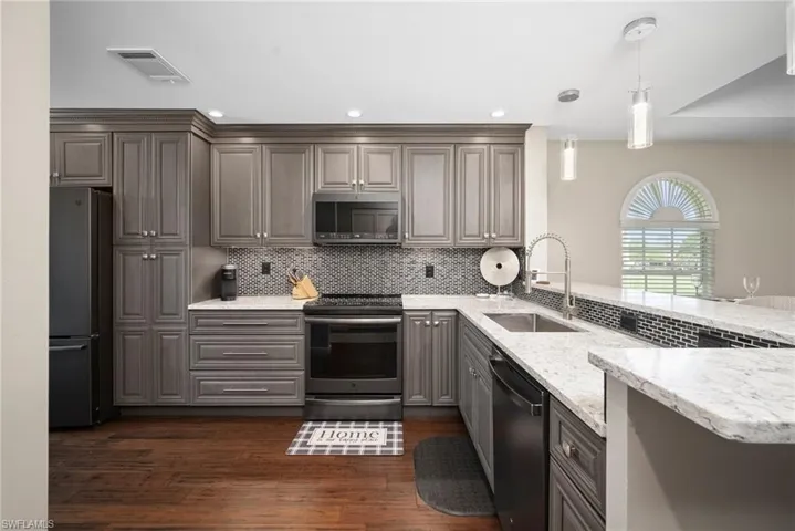 Kitchen with stainless steel appliances, hanging light fixtures, light stone countertops, a peninsula, and gray cabinetry