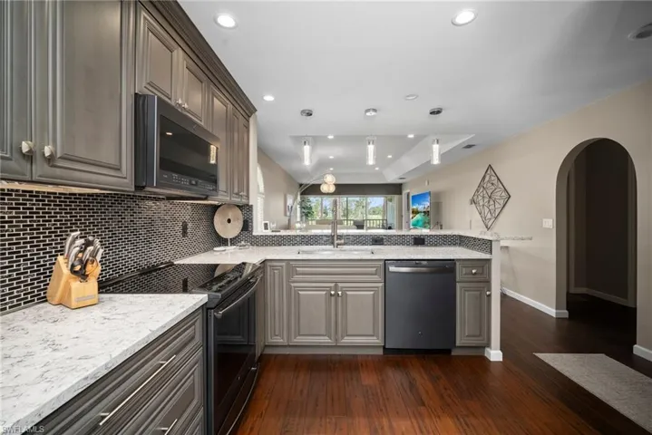 Kitchen with electric stove, arched walkways, black microwave, dishwasher, and light stone countertops