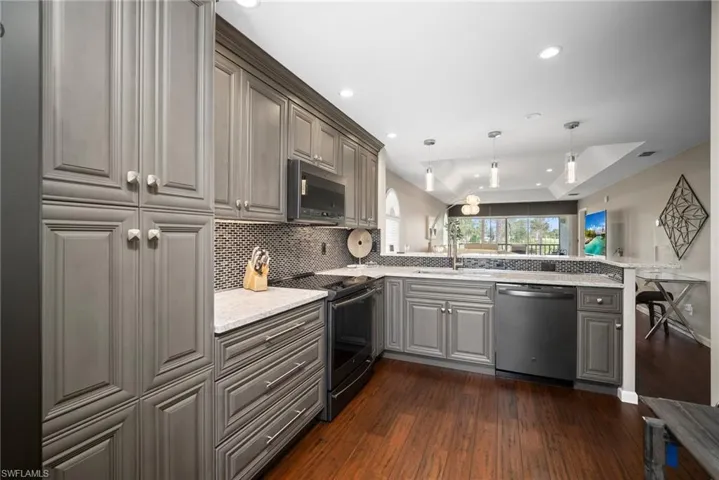 Kitchen featuring stainless steel appliances, gray cabinets, hanging light fixtures, a raised ceiling, and a peninsula