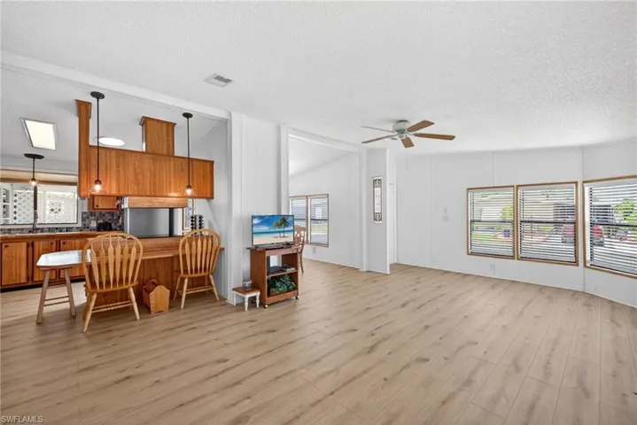 Open concept living area featuring wood-finish flooring, a ceiling fan, and multiple windows with blinds