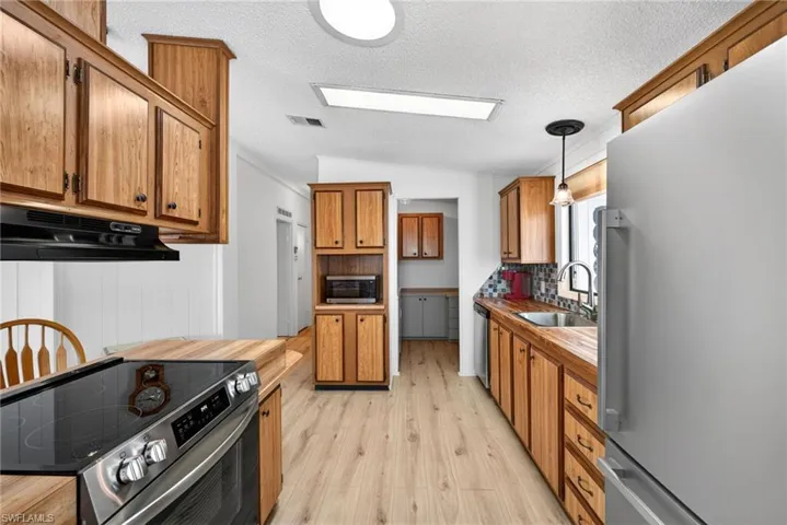 Kitchen featuring wood-finish cabinetry, wood-finish countertops, stainless steel appliances, and wood-finish flooring
