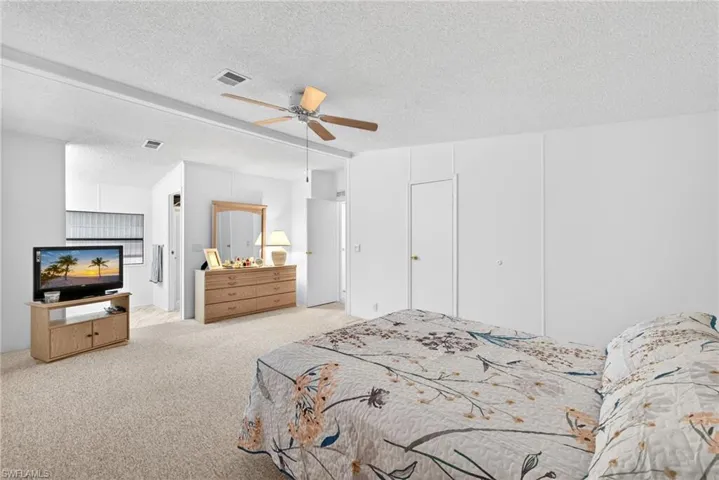Spacious bedroom featuring neutral carpeting, a ceiling fan with light fixture, and white painted walls
