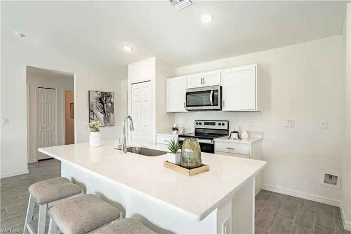 Kitchen with stainless steel appliances, white cabinetry, a breakfast bar, light stone countertops, and lofted ceiling