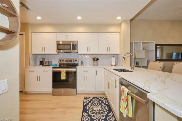 Kitchen featuring sink, white cabinets, light stone countertops, and stainless steel appliances