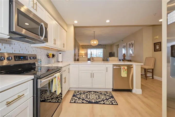 Kitchen with white cabinets, hanging light fixtures, kitchen peninsula, and appliances with stainless steel finishes