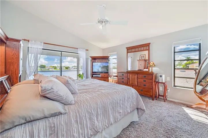 Carpeted bedroom with multiple windows, vaulted ceiling, access to outside, and ceiling fan