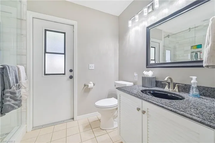 Bathroom featuring a shower with door, vanity, toilet, and tile patterned flooring