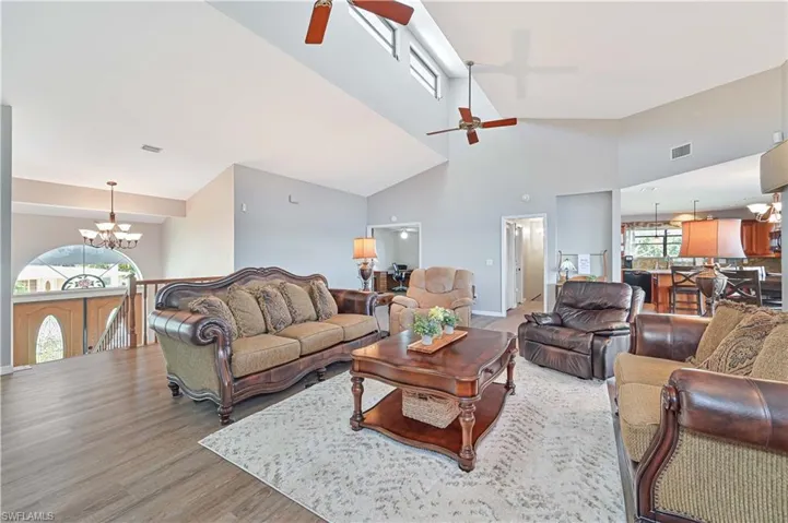 Living room featuring ceiling fan with notable chandelier, high vaulted ceiling, and hardwood / wood-style floors